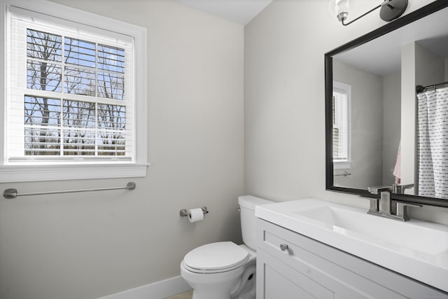 bathroom featuring baseboards, a wealth of natural light, toilet, and vanity