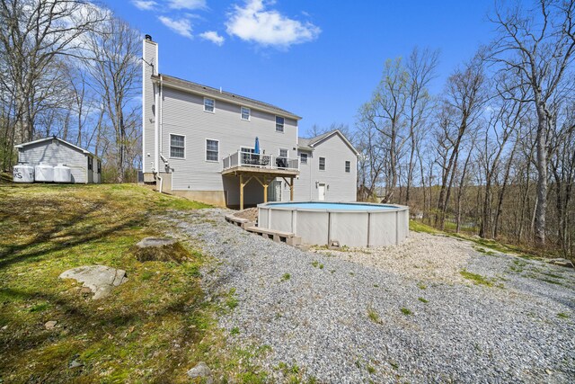 rear view of property featuring an outdoor pool, a chimney, a deck, and an outbuilding