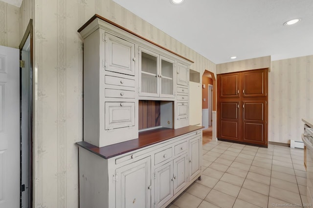 kitchen with glass insert cabinets, arched walkways, dark countertops, and wallpapered walls
