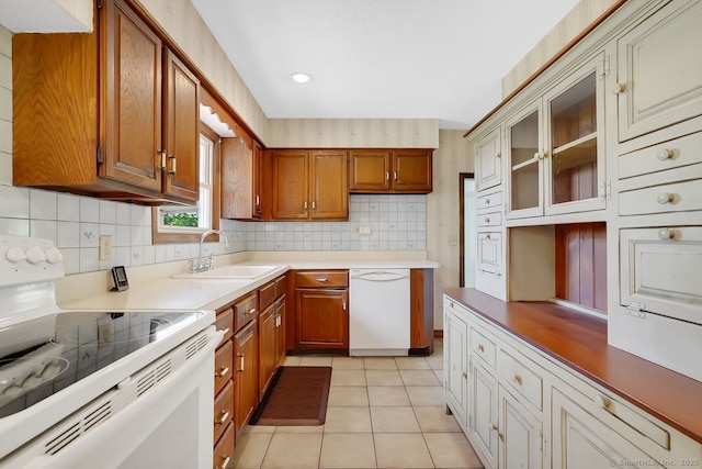 kitchen featuring tasteful backsplash, brown cabinets, a sink, light tile patterned floors, and white appliances