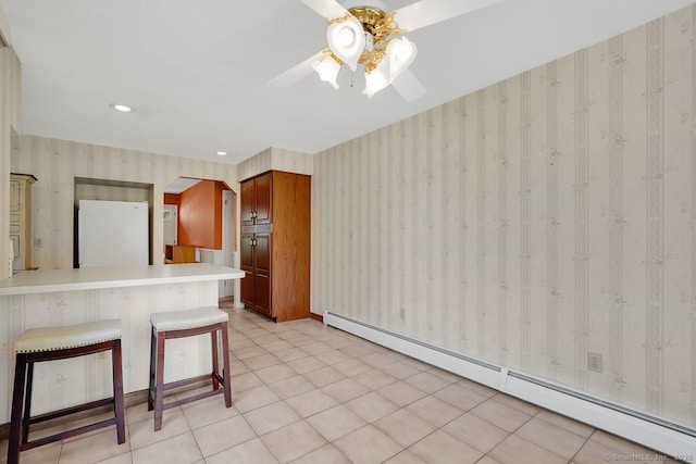 interior space with freestanding refrigerator, a breakfast bar, ceiling fan, baseboard heating, and wallpapered walls