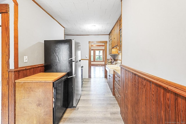kitchen featuring light wood finished floors, freestanding refrigerator, crown molding, light countertops, and wainscoting