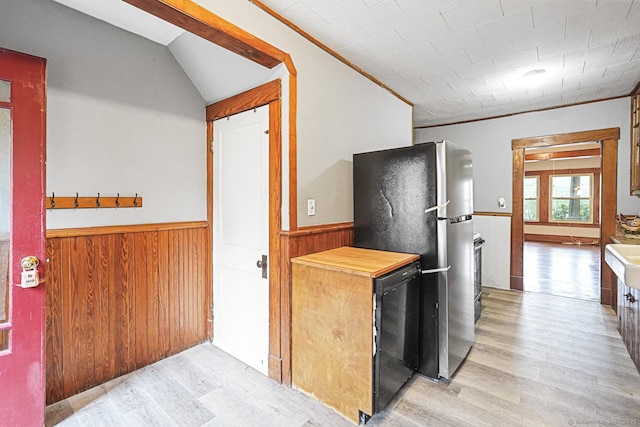 kitchen with freestanding refrigerator, light wood finished floors, a wainscoted wall, wood walls, and crown molding