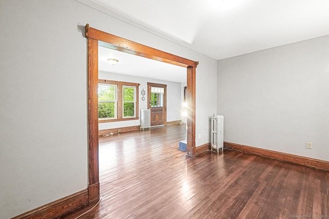unfurnished room featuring radiator heating unit, wood finished floors, and baseboards