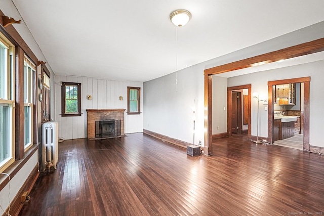 unfurnished living room featuring radiator, hardwood / wood-style flooring, a fireplace, and baseboards