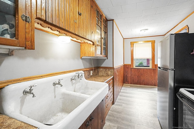 kitchen with electric range, a sink, wainscoting, freestanding refrigerator, and brown cabinets
