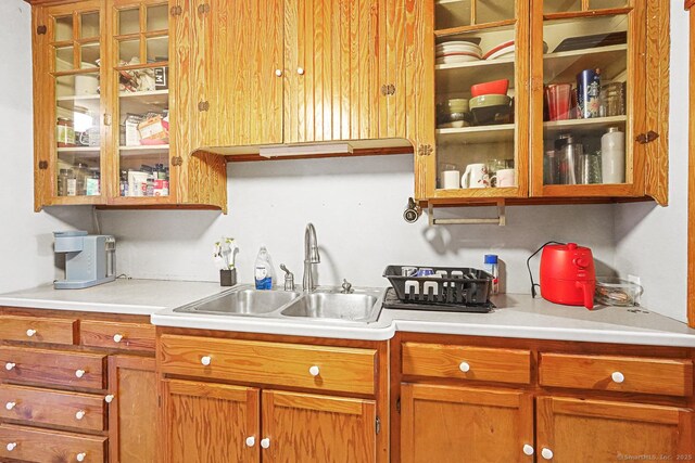 kitchen with a sink, light countertops, glass insert cabinets, and brown cabinetry