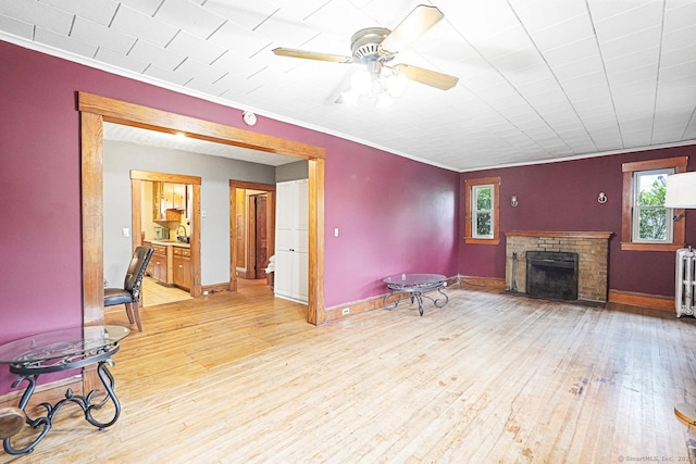 unfurnished living room featuring light wood finished floors, a ceiling fan, a fireplace, baseboards, and ornamental molding