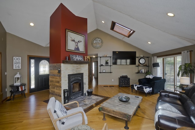 living room with a fireplace, high vaulted ceiling, a skylight, and wood finished floors