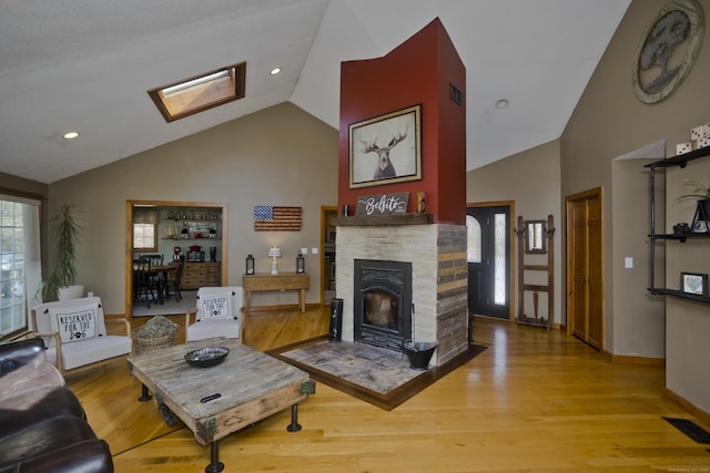 living room featuring a skylight, high vaulted ceiling, visible vents, and wood finished floors