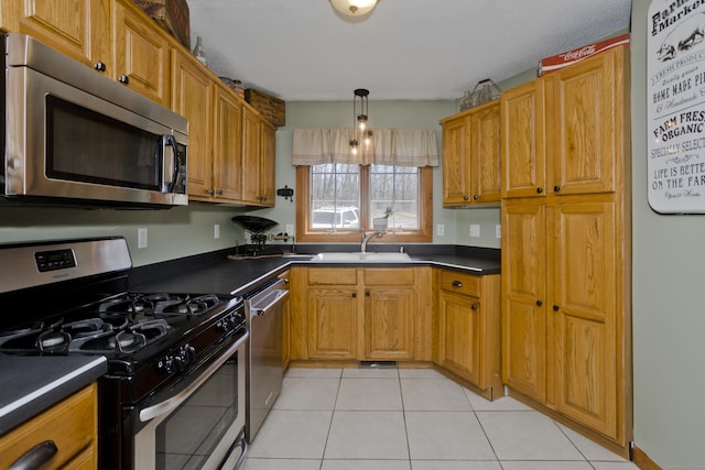 kitchen featuring a sink, brown cabinets, light tile patterned floors, dark countertops, and appliances with stainless steel finishes