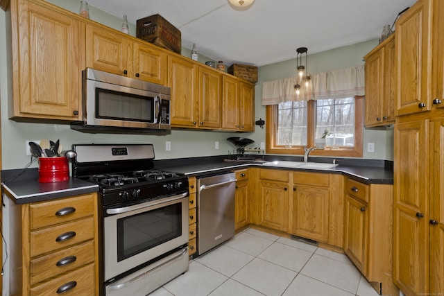 kitchen with light tile patterned floors, a sink, brown cabinets, dark countertops, and appliances with stainless steel finishes