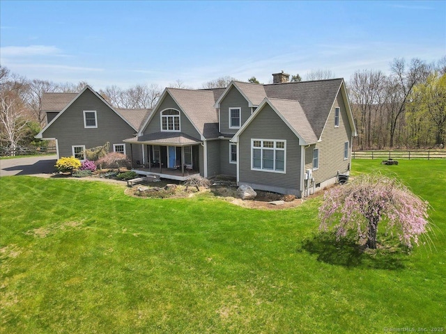 back of house with a shingled roof, covered porch, a lawn, a chimney, and fence