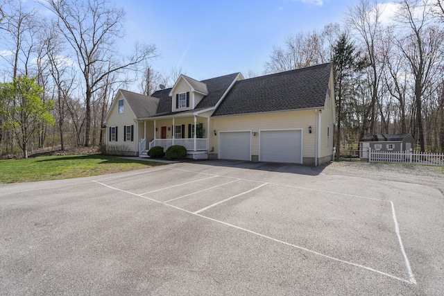 new england style home with covered porch, aphalt driveway, roof with shingles, an attached garage, and fence