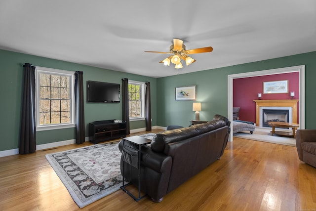 living area featuring baseboards, wood finished floors, a ceiling fan, and a fireplace