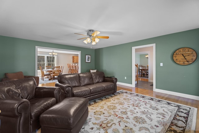 living area featuring baseboards, wood finished floors, and ceiling fan with notable chandelier
