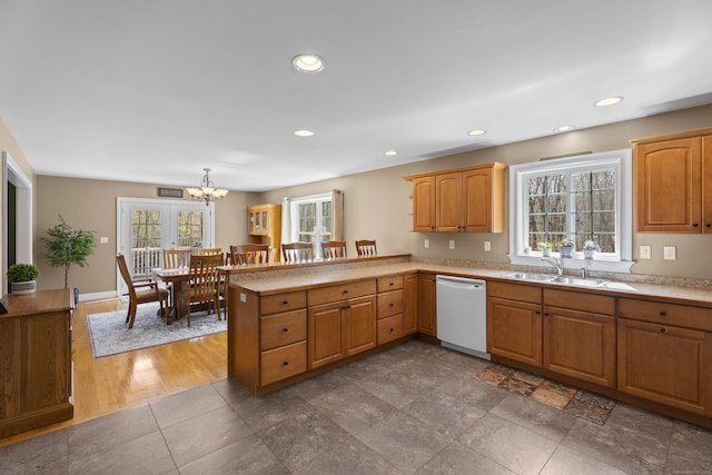 kitchen with a sink, light countertops, white dishwasher, a peninsula, and a notable chandelier