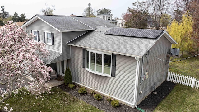 view of home's exterior with central AC, roof mounted solar panels, fence, and a shingled roof