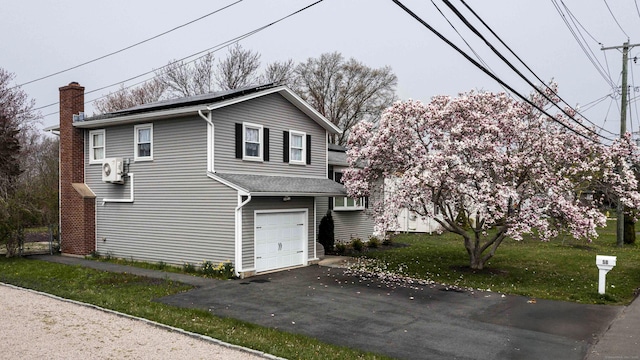 view of front facade with a front lawn, driveway, ac unit, a chimney, and an attached garage