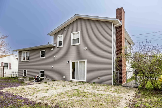 back of house with fence, a chimney, and a gate