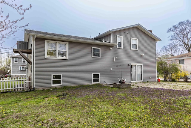 rear view of property featuring central air condition unit, a lawn, and fence