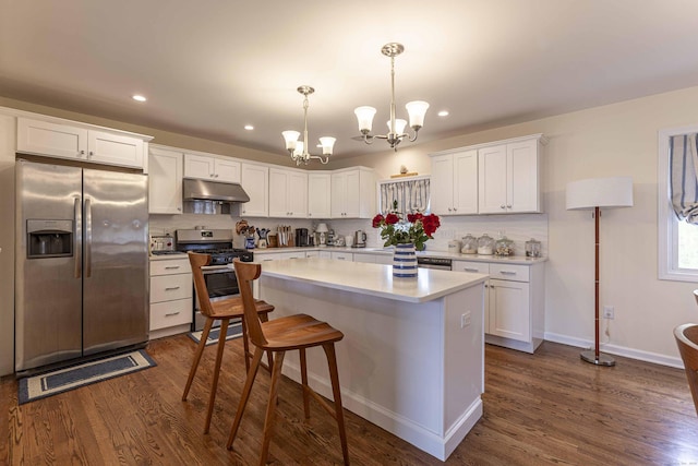 kitchen with a chandelier, under cabinet range hood, appliances with stainless steel finishes, white cabinets, and dark wood-style floors