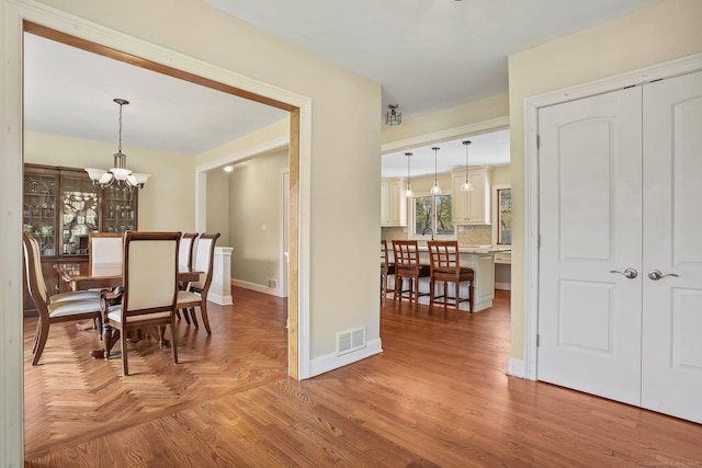 dining space with baseboards, visible vents, an inviting chandelier, and parquet floors