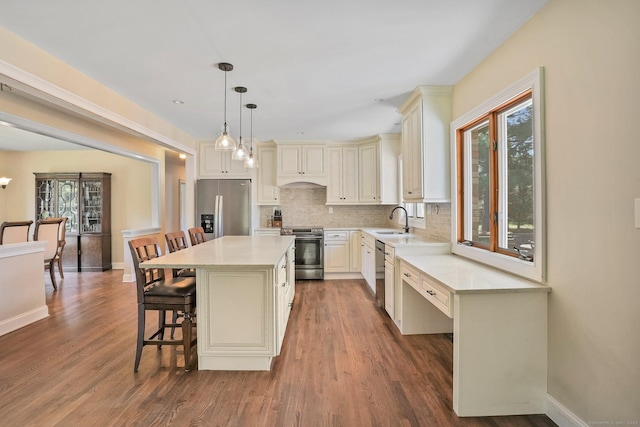 kitchen featuring a sink, appliances with stainless steel finishes, a breakfast bar, light countertops, and backsplash