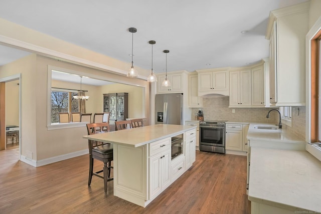 kitchen with wood finished floors, a breakfast bar, stainless steel appliances, light countertops, and a sink