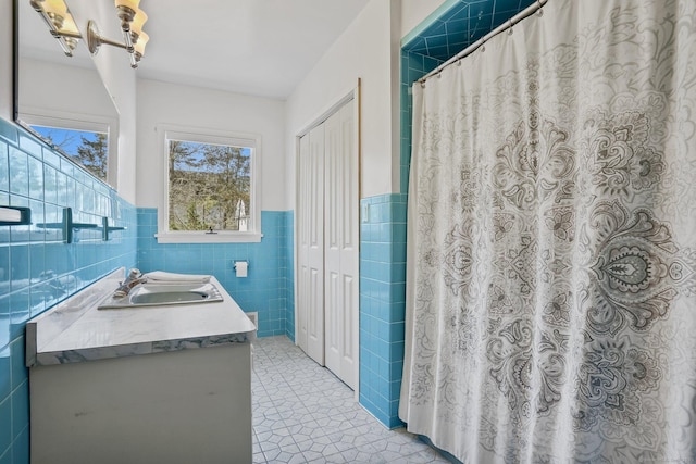 full bath featuring a chandelier, wainscoting, double vanity, tile walls, and a sink