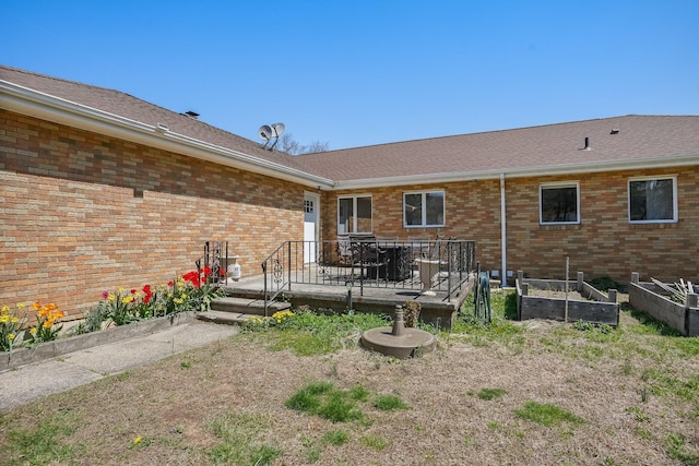 rear view of house featuring a deck, brick siding, a vegetable garden, and roof with shingles