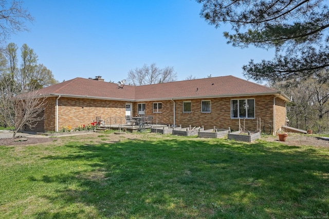 back of house with brick siding, a yard, and a garden