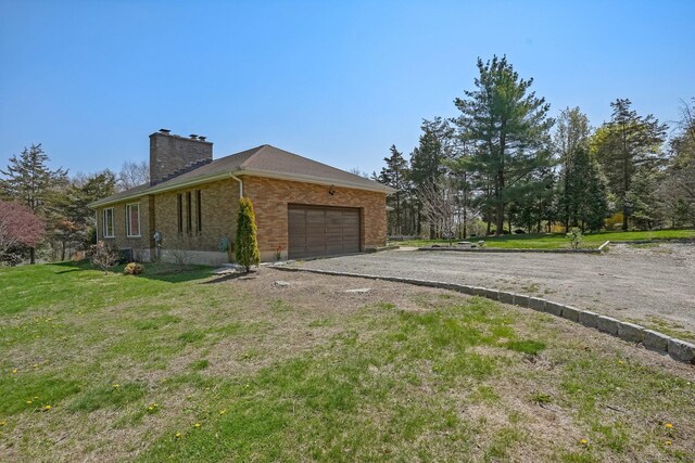 view of property exterior with driveway, a chimney, a lawn, brick siding, and a garage