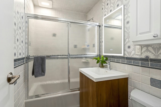 bathroom with vanity, shower / bath combination with glass door, tile walls, toilet, and wallpapered walls