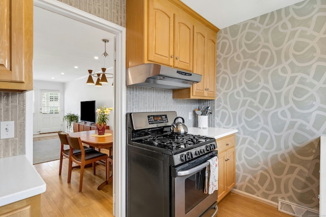 kitchen with light wood finished floors, light brown cabinets, stainless steel range with gas stovetop, wallpapered walls, and under cabinet range hood