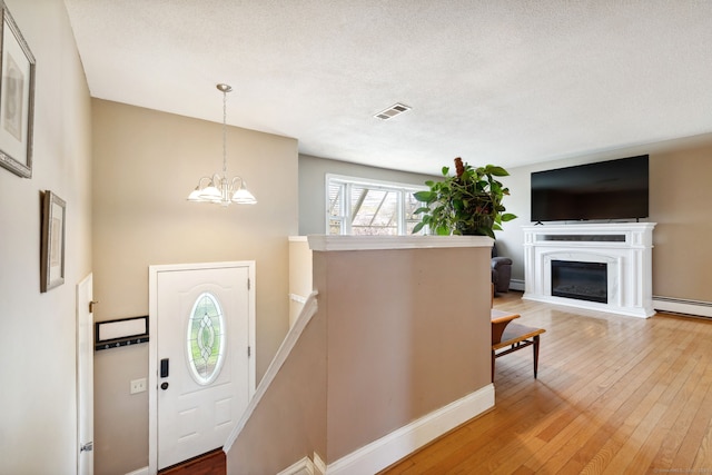 foyer featuring a chandelier, a glass covered fireplace, visible vents, and hardwood / wood-style floors