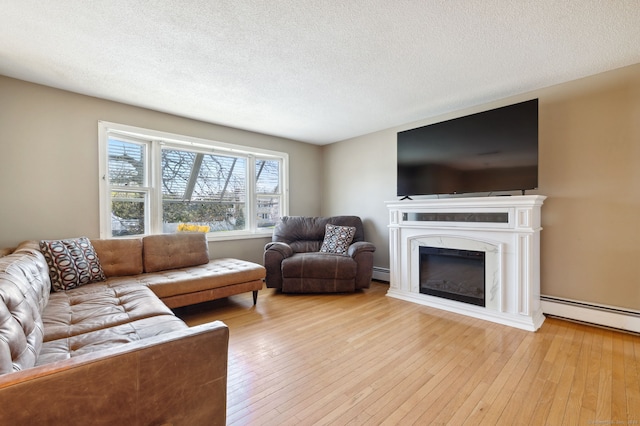 living area featuring a textured ceiling, light wood finished floors, a glass covered fireplace, and a baseboard heating unit