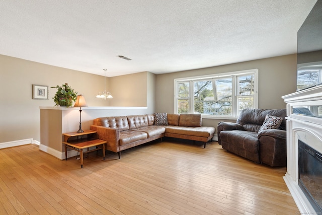 living area featuring light wood-style floors, a chandelier, a glass covered fireplace, baseboards, and visible vents