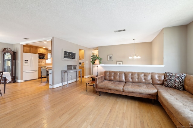 living area featuring a chandelier, a textured ceiling, visible vents, and light wood-type flooring