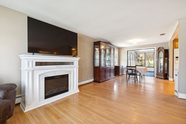 living room featuring a premium fireplace, visible vents, baseboard heating, and light wood-style floors