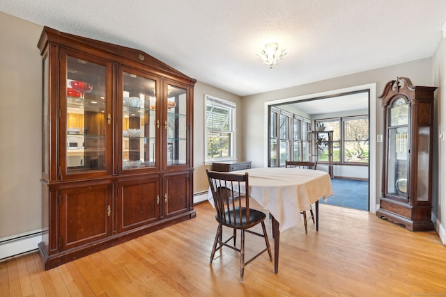dining space with a baseboard radiator, light wood-type flooring, and a textured ceiling