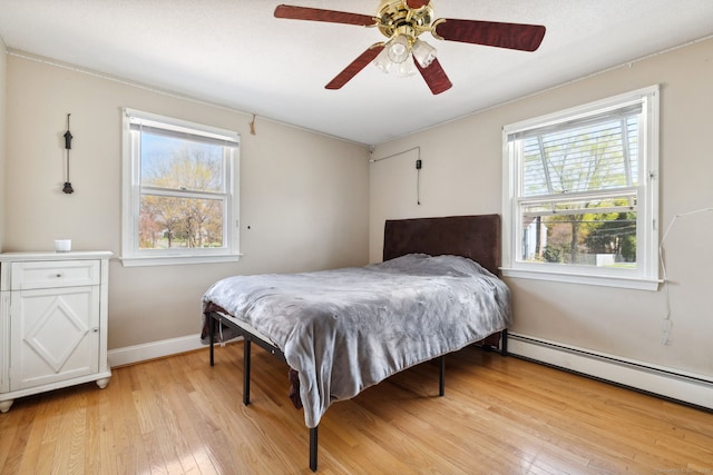 bedroom featuring light wood-style floors, baseboards, ceiling fan, and a baseboard heating unit