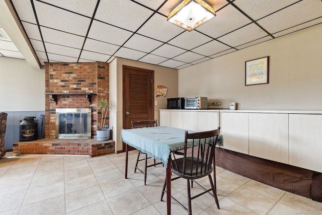 dining area with a paneled ceiling, a brick fireplace, and light tile patterned floors