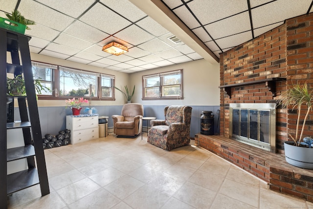 living area with visible vents, wainscoting, a brick fireplace, a paneled ceiling, and tile patterned floors