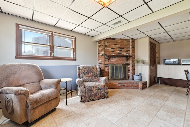 living room featuring light tile patterned floors, a fireplace, a drop ceiling, and visible vents