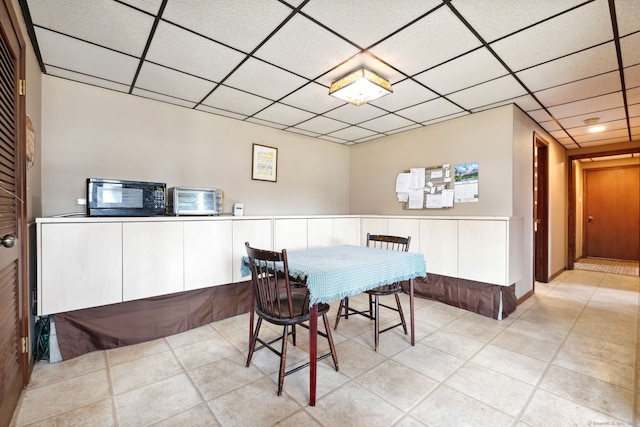 dining space with light tile patterned floors, a drop ceiling, a toaster, and a wainscoted wall