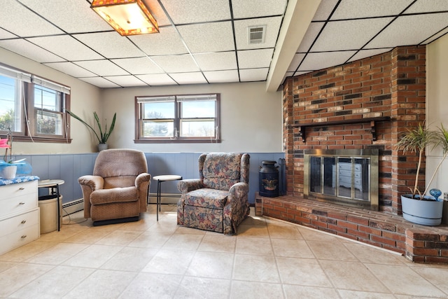 sitting room with visible vents, a baseboard heating unit, a brick fireplace, and a drop ceiling