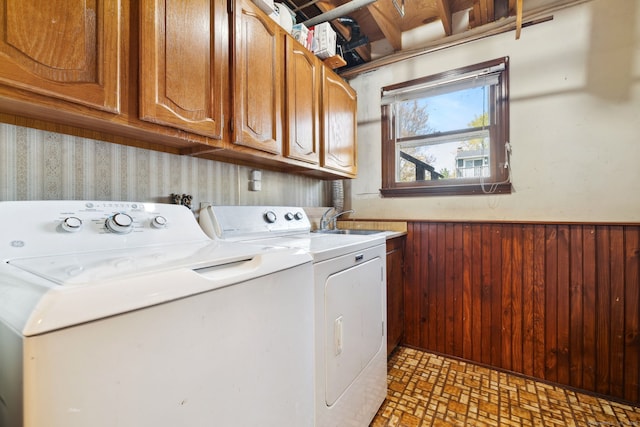 clothes washing area with cabinet space, a sink, separate washer and dryer, wood walls, and a wainscoted wall