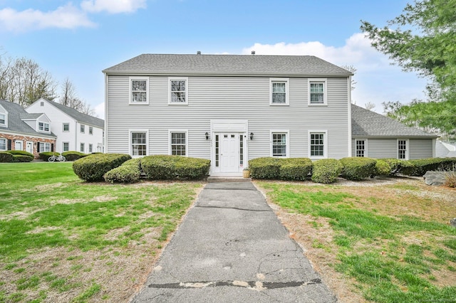 colonial inspired home featuring roof with shingles and a front yard