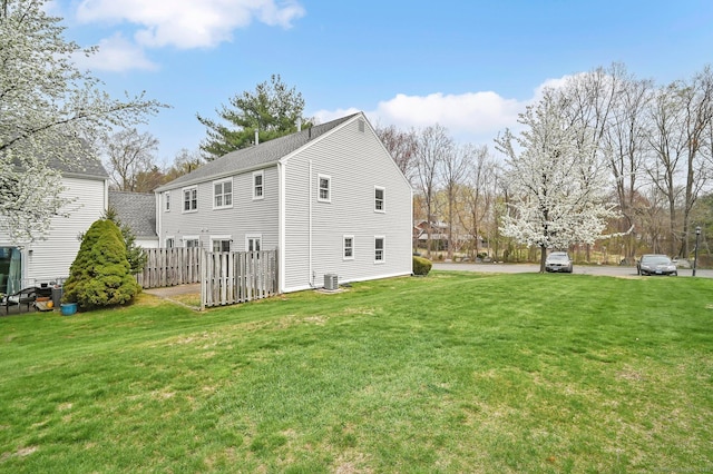 view of side of property with a lawn, fence, central AC unit, and roof with shingles